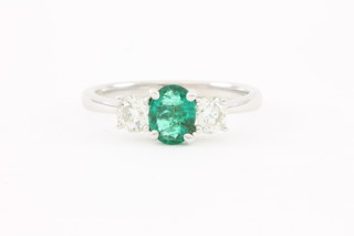 An 18ct white gold claw set oval cut emerald, approx. 0.53ct and 2 stone diamond, approx 0.57ct, dress ring