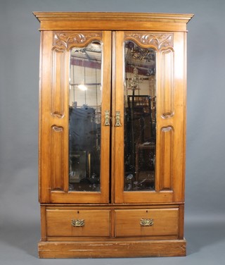A Victorian carved satinwood double wardrobe with moulded cornice enclosed by a pair of shaped bevelled plate mirrored doors, the base fitted 2 long drawers, raised on a platform base 77"h x 50 1/2"w x 20"d 
