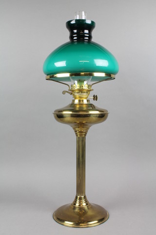 A brass oil lamp reservoir raised on a reeded glass column with clear glass chimney and green shade 