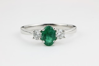 An 18ct white gold 3 stone ring, the centre oval cut emerald approx. 0.74ct flanked by single brilliant cut diamonds approx. 0.33ct