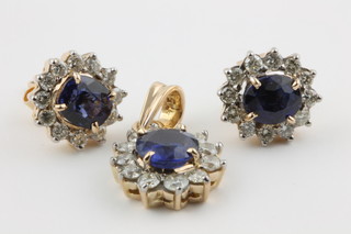 A yellow gold sapphire and diamond suite comprising a pair of earrings, the oval sapphire surrounded by 12 brilliant cut diamonds with a matching pendant