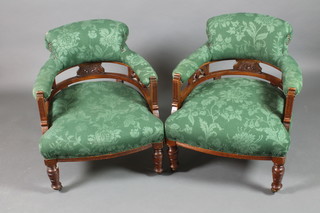 A pair of Victorian walnut tub back chairs upholstered in green material, raised on turned supports