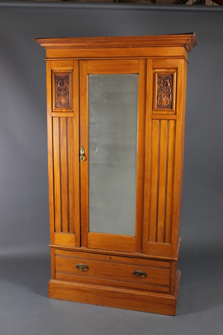 An Edwardian satinwood wardrobe with moulded cornice enclosed by a bevelled plate panelled mirrored door, having carved panels to the side, the base fitted 1 long drawer, raised on a platform base 82"h x 45 1/2"w x 21"d 