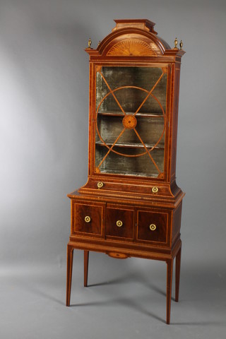 A handsome and fine quality Edwardian inlaid mahogany Sheraton style display cabinet, the arched upper section inlaid a fan, the interior fitted shelves with plush lining enclosed by an astragal glazed door above a concave drawer, the base crossbanded with satinwood, fitted 1 short drawer flanked by a pair of cupboards, raised on square tapering supports 80 1/1"h x 30"w x 16"d 