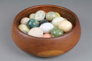 A turned wooden bowl containing a collection of hardstone hand cooler eggs