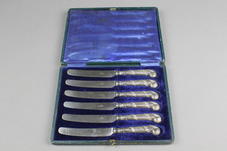 A set of 6 cased silver handled butter knives with pistol grip repousse handles