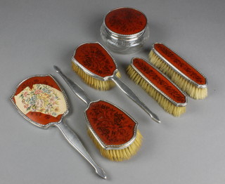 A silver backed dressing table set comprising 2 hair brushes, 2 clothes brushes, a hand mirror, powder bowl/toilet jar with embroidered needlepoint panels 