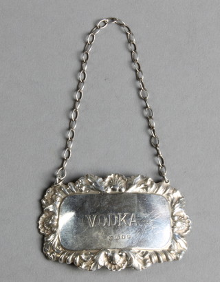 A repousse silver Vodka label with scroll decoration 