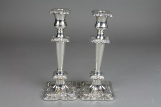 A pair of silver candlesticks with repousse floral and scroll decoration with tapered bodies on stepped bases 11"