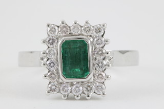 A 14ct white gold rectangular cut emerald and diamond cluster ring, the centre stone approx 1ct surrounded by 18 brilliant cut diamonds, approx 0.5ct 