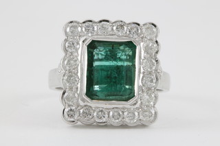 An 18ct white gold rectangular cut emerald and diamond cluster ring, the centre stone approx. 0.60ct surrounded by 20 brilliant cut diamonds, approx 1.2ct