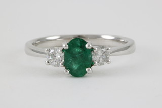An 18ct white gold 3 stone ring, the centre oval cut emerald approx. 0.74ct flanked by single brilliant cut diamonds approx. 0.33ct