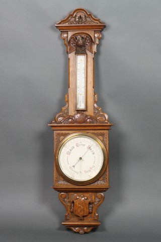 An Edwardian aneroid barometer and thermometer contained in a heavily carved oak case