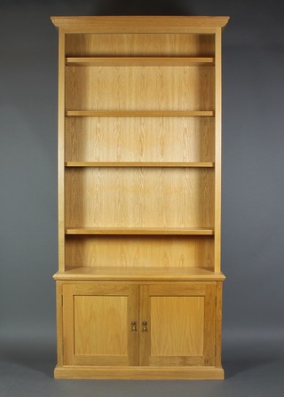 A light oak library bookcase, the upper section with moulded cornice the interior fitted adjustable shelves, the base fitted a double cupboard enclosed by a pair of panelled doors, raised on a platform base (in one piece) 95"h x 47"w x 14"d  