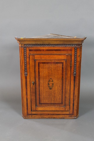 A Georgian III oak hanging corner cabinet with moulded cornice, the interior fitted shelves enclosed by a panelled door with Prince of Wales feather inlay to the centre 39"h x 30"w x 17"d