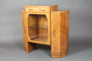 An Art Deco walnut display cabinet, the upper section fitted a drawer above a cupboard enclosed by a shaped panelled glass door, having cupboards to the sides with chromed handles 39"h x 39 1/2"w x 14"d