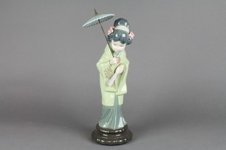 A Lladro figure of a Japanese lady holding a parasol and a fan on a raised faux hardwood stand 14"
