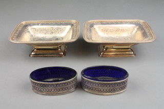 A pair of oval Adam style silver plated table salts with blue glass liners and a pair of plated dishes