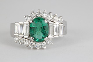 An 18ct white gold emerald and diamond dress ring, the centre set an oval cut emerald approx. 1.5ct flanked by 3 stepped cut baguette diamonds surrounded by 14 brilliant cut diamonds