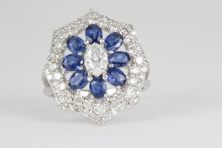 A 14ct white gold sapphire and diamond open cluster ring, the centre diamond flanked by 8 oval cut sapphires enclosed in a stepped brilliant diamond border