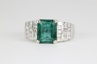An 18ct white gold emerald and diamond ring, the rectangular cut emerald approx. 4.2ct flanked by 3 stepped tiers of 14 Princess cut diamonds approx. 1.0ct