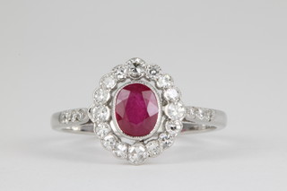 An 18ct white gold ruby and diamond cluster ring, the centre oval cut ruby approx. 0.7ct surrounded by 16 brilliant cut diamonds with 3 stone diamond set shoulders 