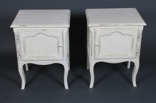 A pair of French white painted oak bedside cabinets enclosed by arch panelled doors, raised on cabriole supports 24 1/2"h x 18 1/2"w x 15"d 