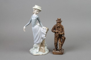 A Lladro figure of a lady leaning beside a tree stump 11", a carved wooden figure of a gentleman 8" 
