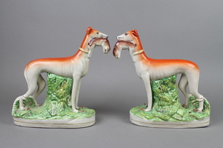 A pair of Staffordshire figures of standing greyhounds with hares in their mouths, on raised bases 10" 