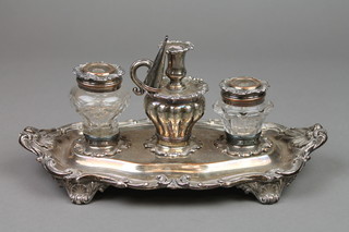 A 19th Century Rococo plated ink stand with fancy scroll and shell rim with 2 cut glass bottles and centre miniature chamber stick, on scroll feet, 11" 