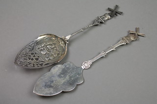 2 Dutch silver servers, one with pierced decoration and revelling scene with windmill terminal, the other with a fancy scroll stem and windmill terminal, approx 108 grams 