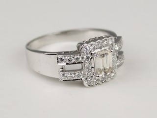 An 18ct white gold diamond ring, the centre emerald cut stone surrounded by brilliants in an open shank, size P
