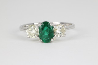 An 18ct white gold emerald and diamond ring, the centre oval cut emerald approx. 0.75ct flanked by single diamonds, each approx. 0.4ct, size M 1/2 