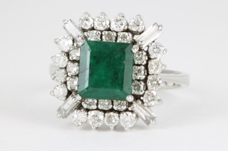 An 18ct white gold emerald and diamond cluster ring, the centre emerald approx 3cts surrounded by 28 brilliant cut diamonds interspersed with 4 baguette cut diamonds, size 0 1/2 