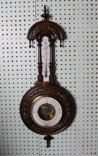 An aneroid barometer and thermometer with paper dial contained in a carved walnut wheel case, (brass bezel f)
