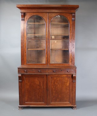 A Victorian mahogany bookcase on cabinet, the upper section with moulded cornice, the interior fitted shelves enclosed by arch panelled doors, the base fitted 2 long drawers above a double cupboard with vitruvian scrolls to the side, raised on bun feet 88"h x 49" w x 20"d