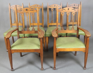 A set of 6 Art Nouveau pierced oak stick and rail back dining chairs with upholstered seats, raised on square tapering supports 