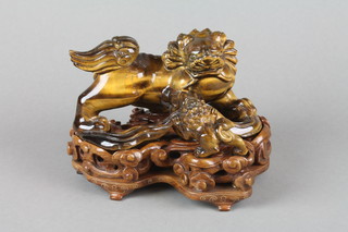 An early 20th Century Chinese tiger's eye carving of a shi-shi with pup on a raised scroll base, on a carved hardwood base decorated with flowers