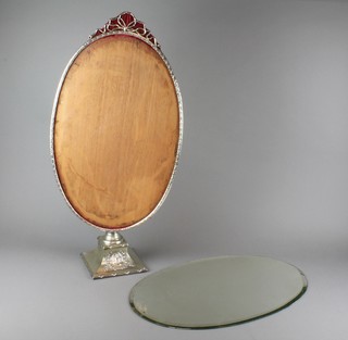 An oval bevelled glass dressing table mirror in a repousse silver frame with open ribbon crest, on a plated classical style stand with classical figures amongst flowers 