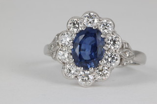 An 18ct white gold sapphire and diamond cluster ring, the centre oval sapphire approx. 1.5ct surrounded by 10 brilliant cut diamonds approx 0.5ct, size M 1/2