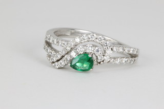 A 14ct white gold emerald and diamond fancy ring with a pear cut emerald surrounded by brilliant cut diamonds