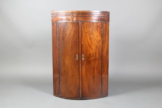 A Georgian mahogany bow front hanging corner cabinet fitted shelves enclosed by panelled doors, with moulded cornice, 40"h x 17"d x 26"w 