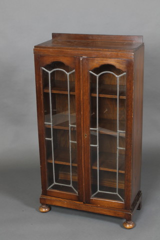 A 1930's Art Deco oak display cabinet, fitted adjustable shelves enclosed by arched lead glazed panelled doors, raised on bun feet 44"h x 23"w x 10"d 