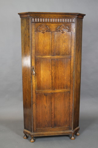 A 1930's carved oak corner hall wardrobe with arcaded decoration enclosed by a panelled door, raised on bun feet 96"h x 35"w x 22"d (old worm to base)