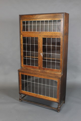 An oak Globe Wernicke style bookcase, the upper section fitted a cupboard enclosed by a sliding glazed panelled door above a cupboard enclosed by panelled doors with sliding panelled door beneath, with bobbin turned decoration, 68"h x 34"w x 15"d