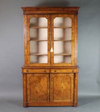 A Victorian inlaid figured walnut display cabinet on cabinet, the upper section with moulded cornice, fitted shelves enclosed by glazed panelled doors, the base fitted 2 long drawers above a double cupboard with columns to the sides, 82", x 47"w x 16"d