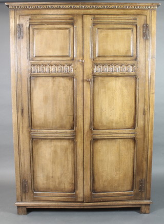 A carved oak wardrobe with moulded cornice enclosed by panelled doors with arcaded decoration raised on bun feet 70"h x 48"w x 20"d  