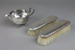 A pair of silver clothes brushes and a plated cream jug 