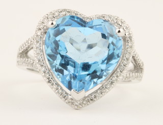 A 14ct white gold blue Topaz heart shaped ring, the centre stone approx. 6.75ct surrounded by brilliant cut diamonds on an open diamond set shank, approx 0.5ct, size M