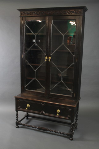 A carved oak bookcase on stand, the upper section with moulded and carved cornice, fitted adjustable shelves enclosed by lead glazed panelled doors, the base fitted 1 long drawer, raised on spiral turned and bun feet 69"h x 36"w x 15"d 